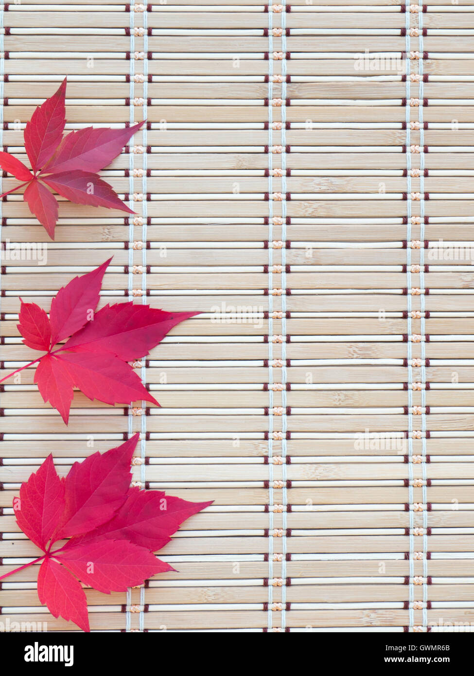 Tres hojas de otoño rojo sobre el bambú mat Foto de stock