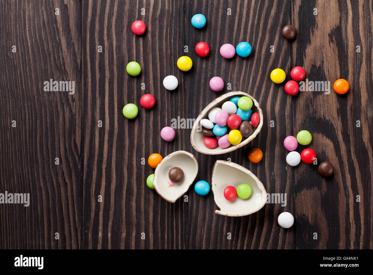 Caramelos de colores y huevo de chocolate sobre fondo de madera. Vista superior con espacio de copia Foto de stock