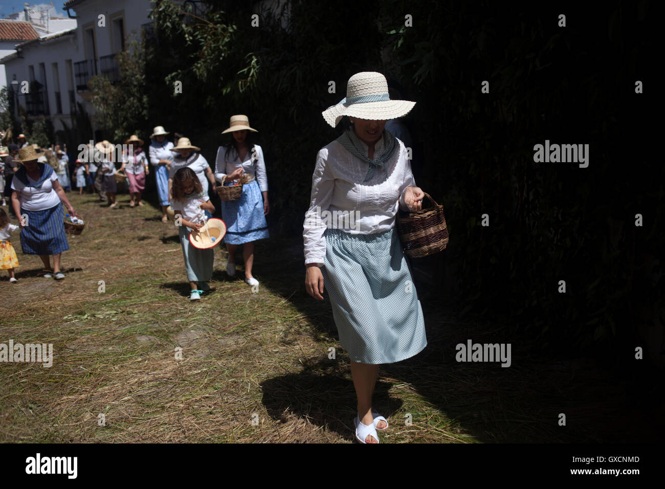 Mujeres vestidas como recolectores caminando en una calle cubierta con juncia durante la celebración religiosa del Corpus Christi en El Gastor, Sierra Foto de stock