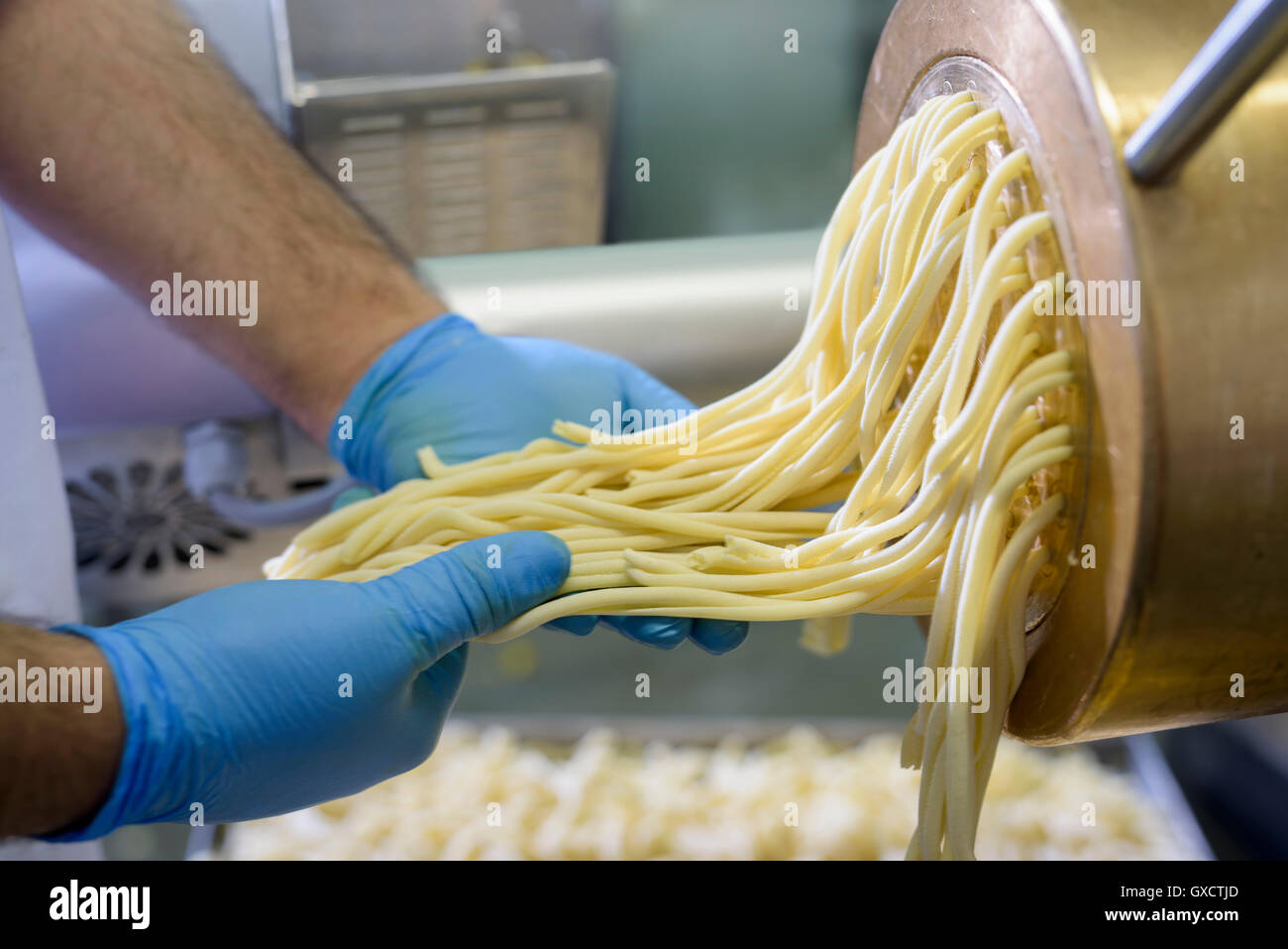 Trabajador con espaguetis que sale de la máquina en la fábrica de pasta Foto de stock