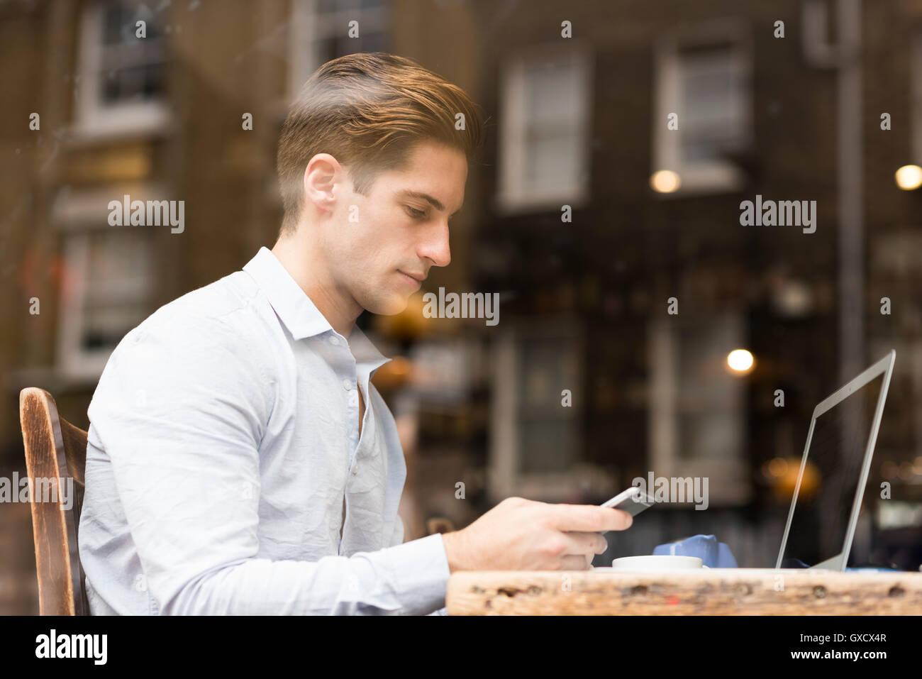 La vista de la ventana del joven empresario de smartphone de lectura de textos en el cafe Foto de stock