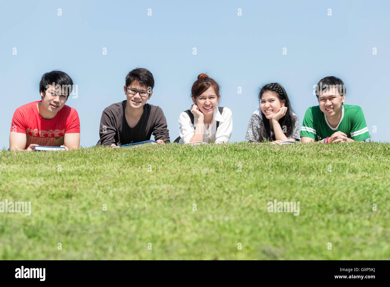 Grupo de amigos que estudian en la escuela al aire libre en el parque.Cinco asiáticas estudiante de la high school secundaria acostado en el pasto en la escuela. Foto de stock