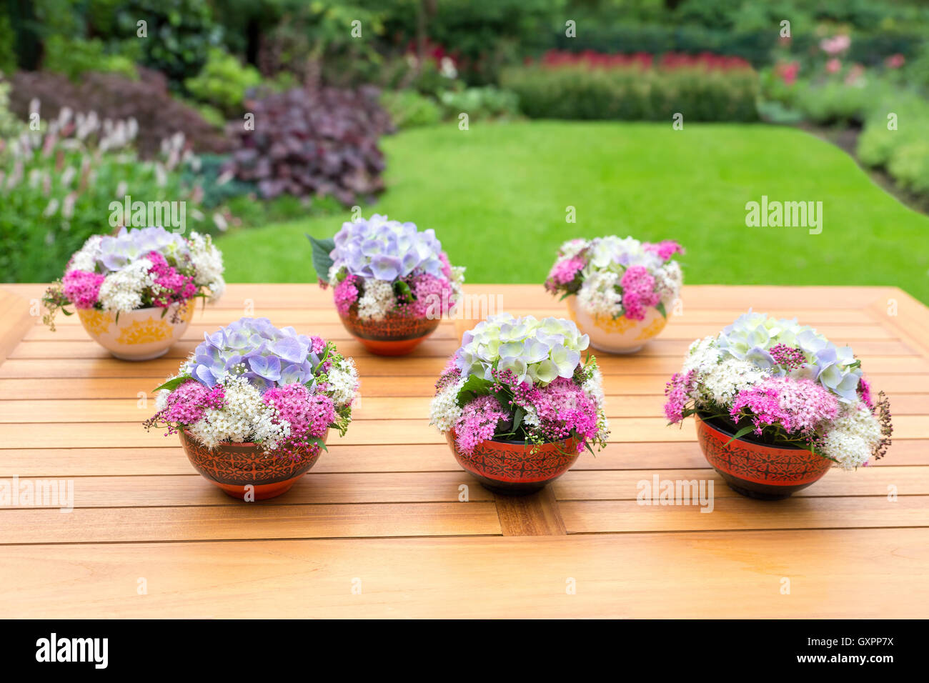 Jarrones con flores floreciendo en mesa de teca al aire libre en el jardín Foto de stock