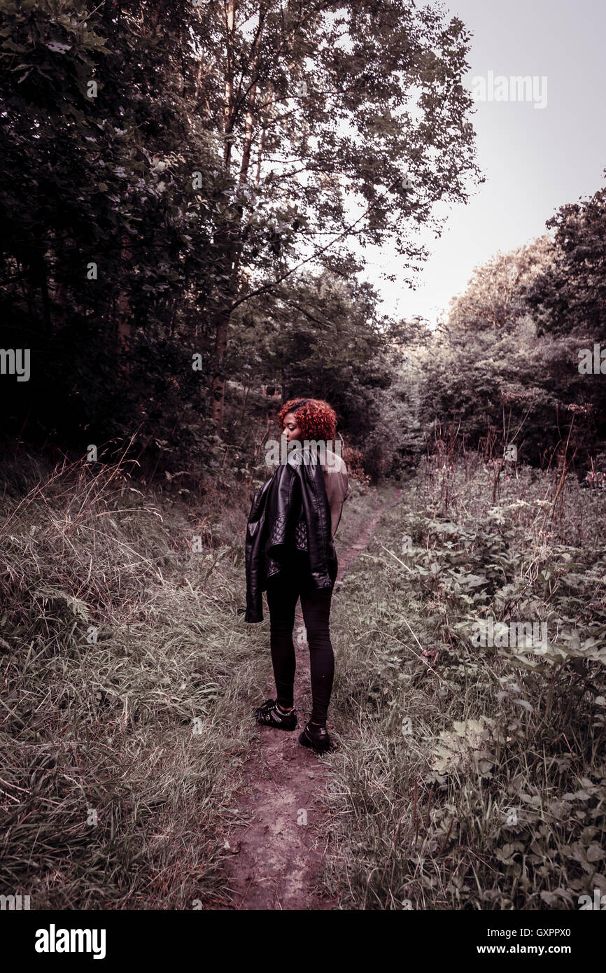 Una hermosa adolescente negro se convierte en un trazado como ella camina en el bosque, colores desaturados. Foto de stock
