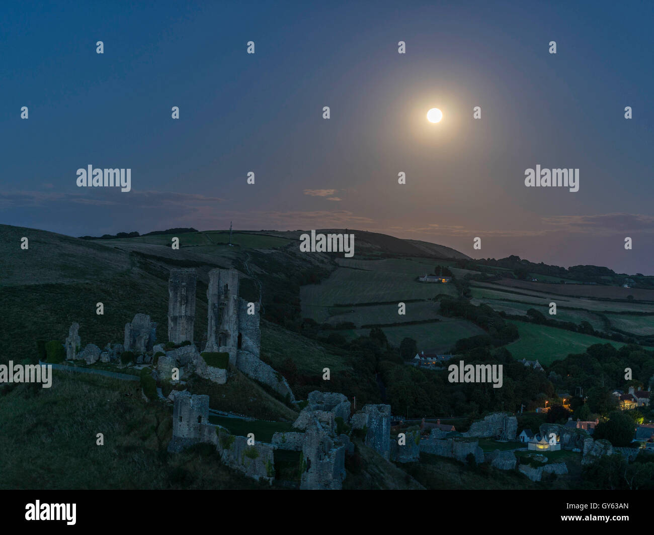 Paisaje representando a finales del verano la cosecha aumentando la luna llena en el castillo Corfe, en Dorset, Reino Unido Foto de stock