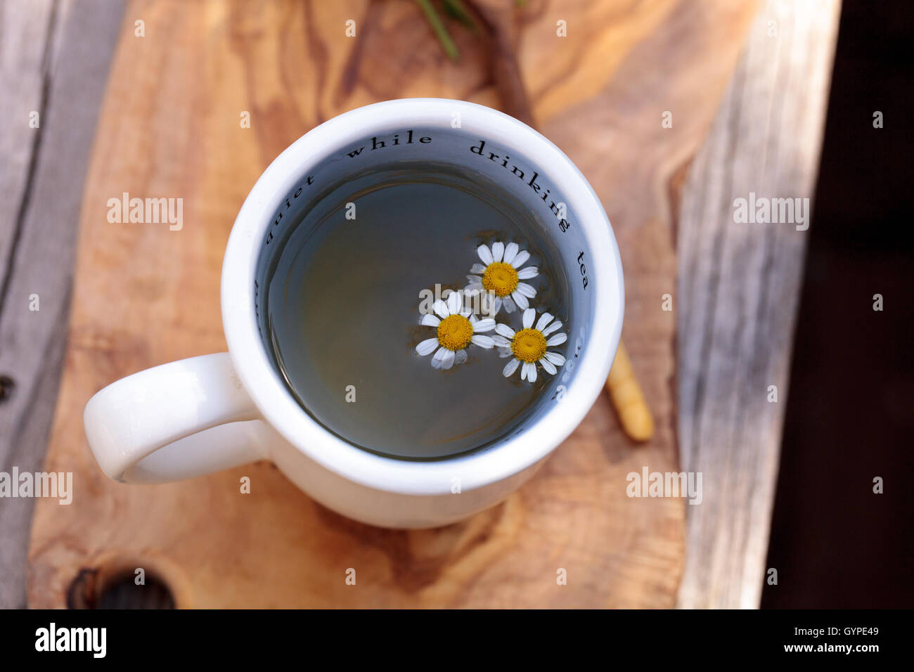 Un té de manzanilla con daisy flores de manzanilla en una taza blanca caliente sobre una placa de corte rústico de madera y una cuchara. Este remedio casero es Foto de stock