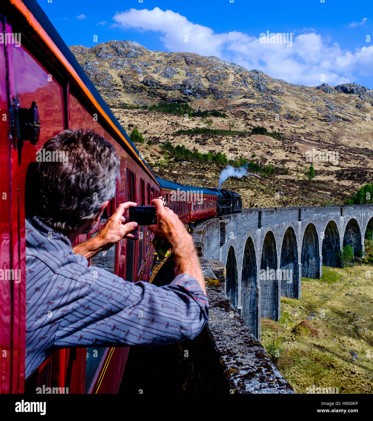 El hombre se inclina por la ventana teniendo una imagen de 'El tren histórico' para el tren de vapor jacobita conduciendo sobre el Viaducto de Glenfinnan Foto de stock