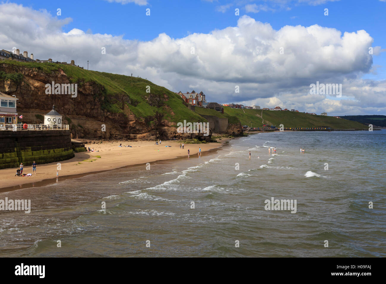 Bañistas en la playa de West Cliff, respaldada por acantilados de hierba en verano, Whitby, North Yorkshire, Inglaterra, Reino Unido, Europa Foto de stock