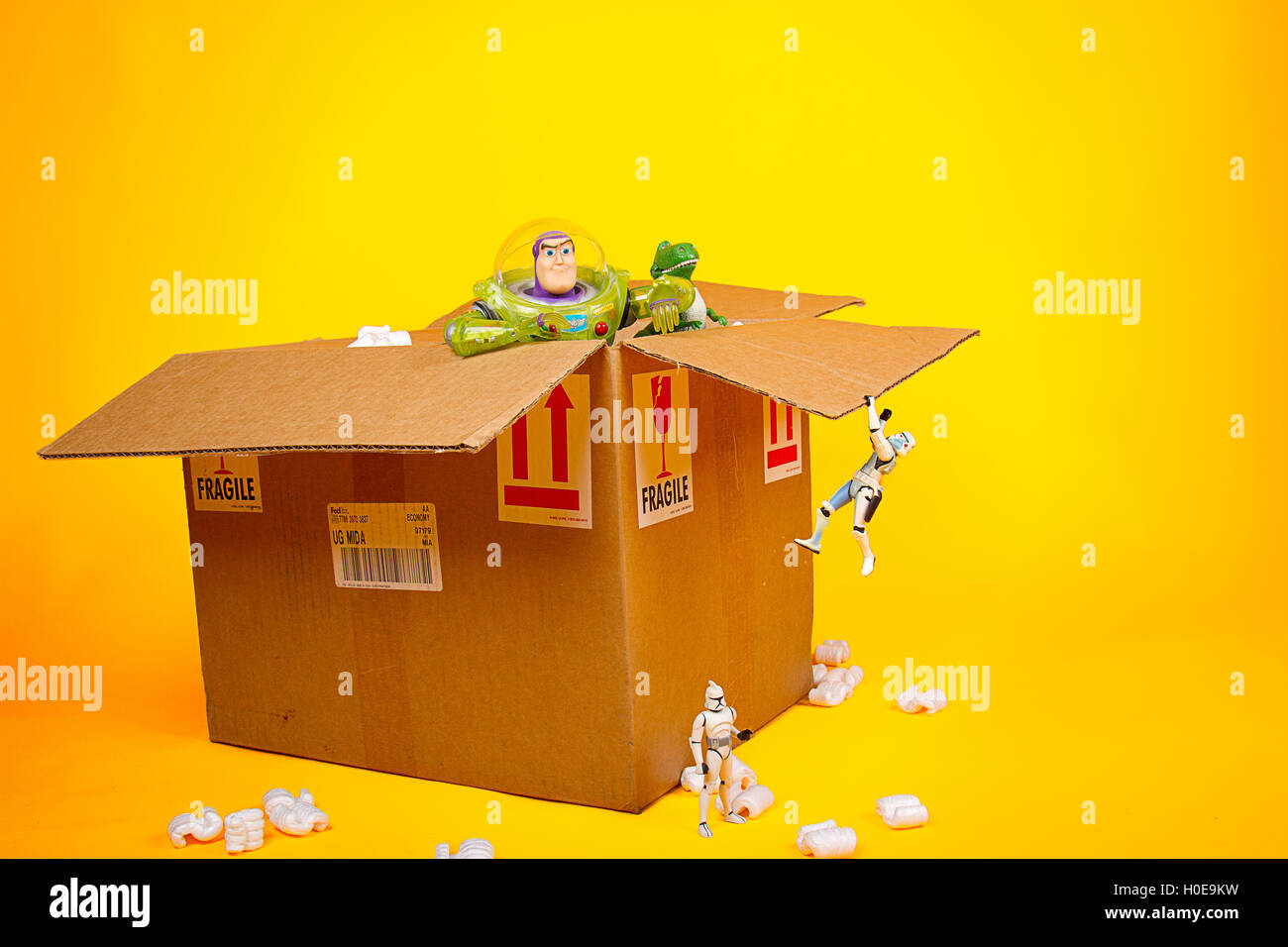 Una escena humorística de juguetes (Starwars y toy story caracteres) unboxing de un paquete de verificación aislada en un fondo amarillo. Foto de stock