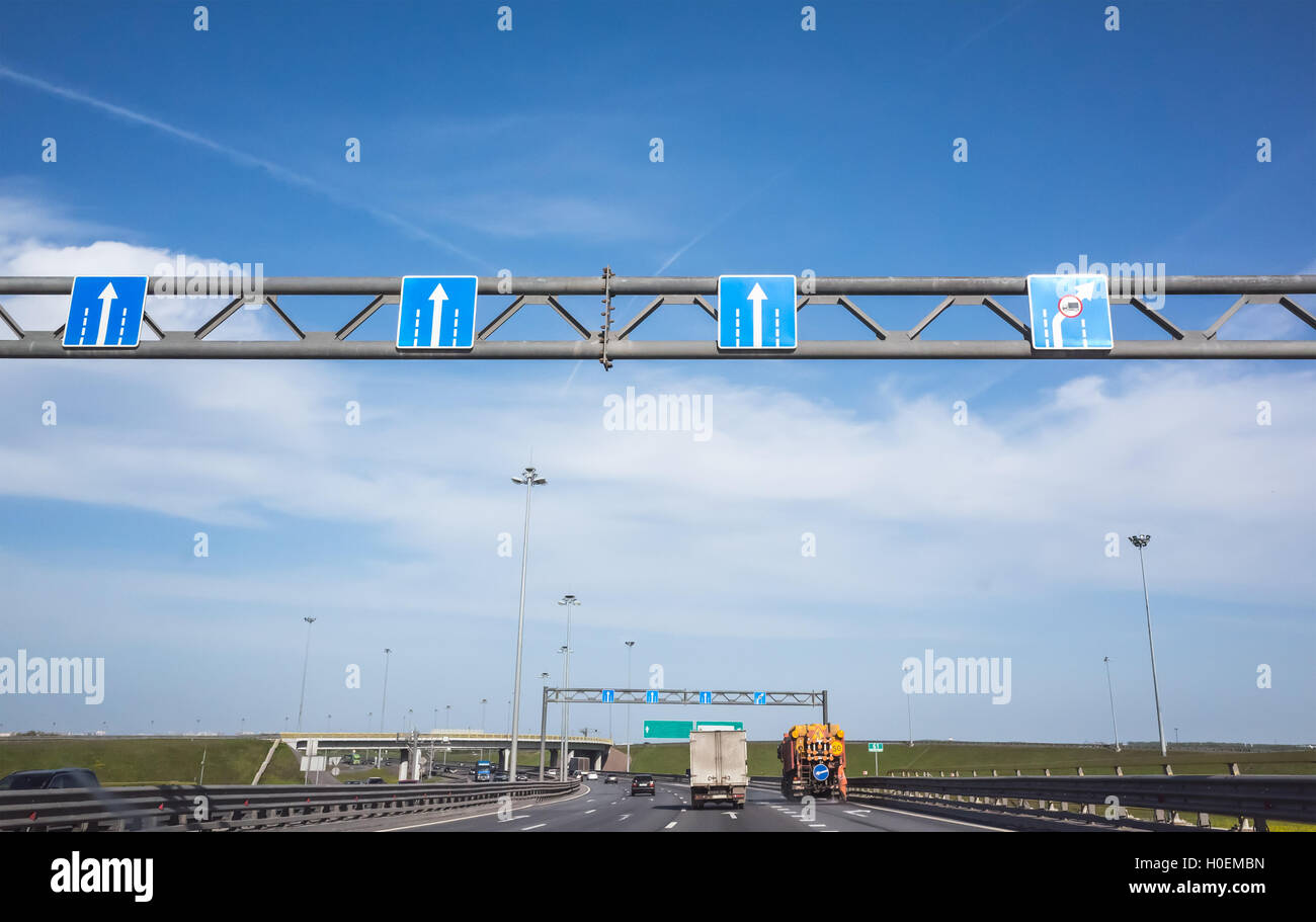 Amplia equipos viales, señales de carretera azul con flechas blancas muestra la dirección del movimiento a lo largo de los carriles de tráfico Foto de stock