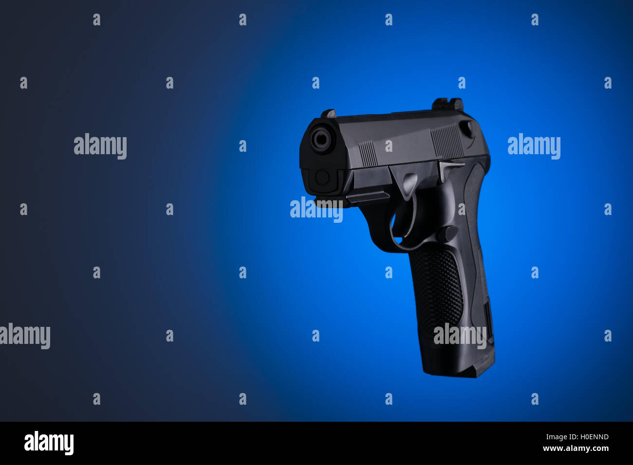 Pistola negra lateralmente aislado sobre fondo azul. Foto de stock