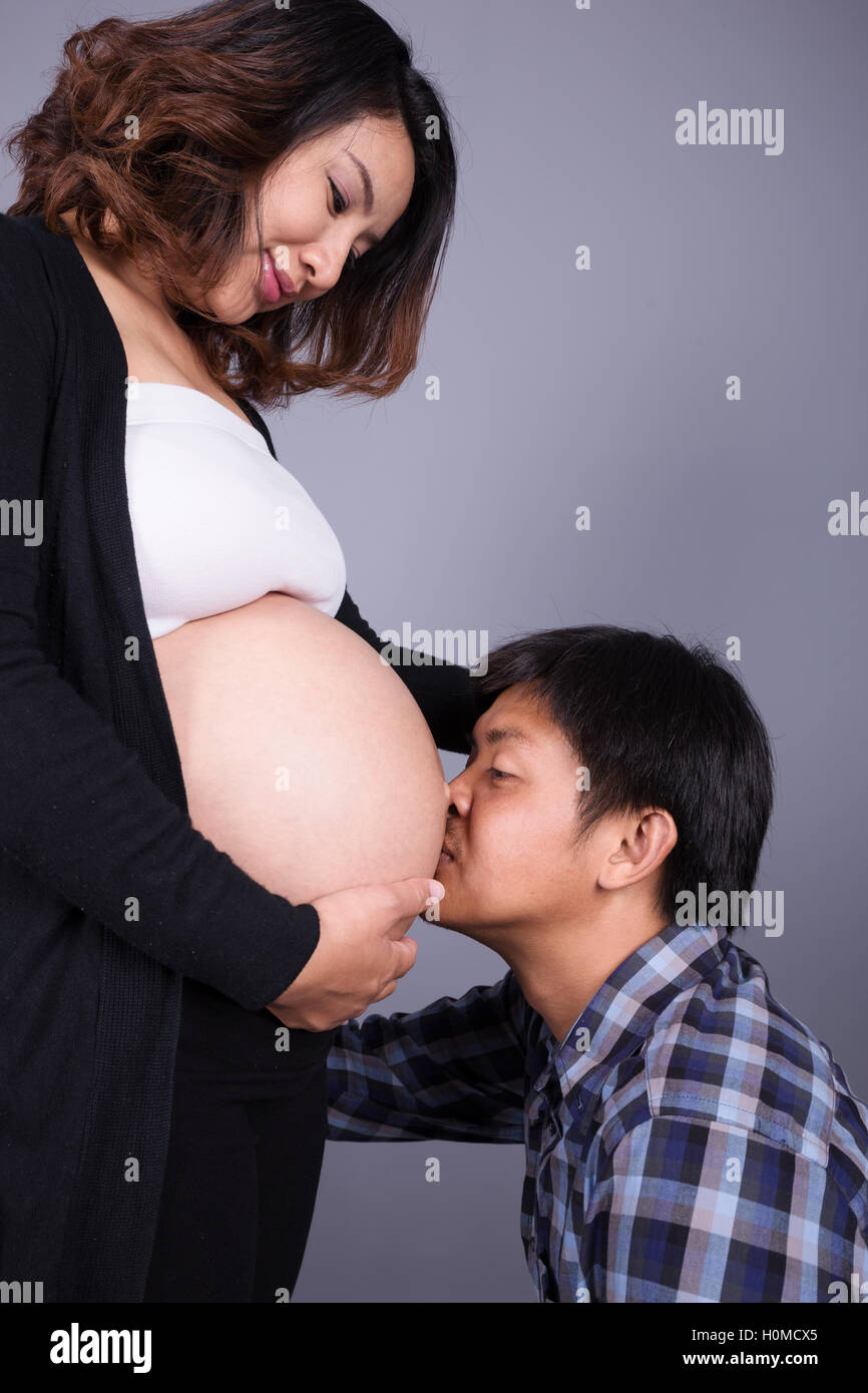 Joven besando a su esposa embarazada del vientre gris sobre fondo de pared Foto de stock