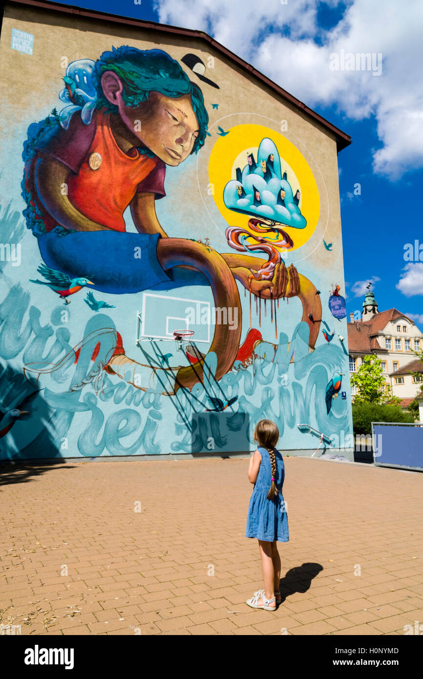 Un colorido graffity con motivo de cómic está pintada en una pared de la casa, una niña está mirando hacia arriba, Würzburg, Baviera, Alemania Foto de stock