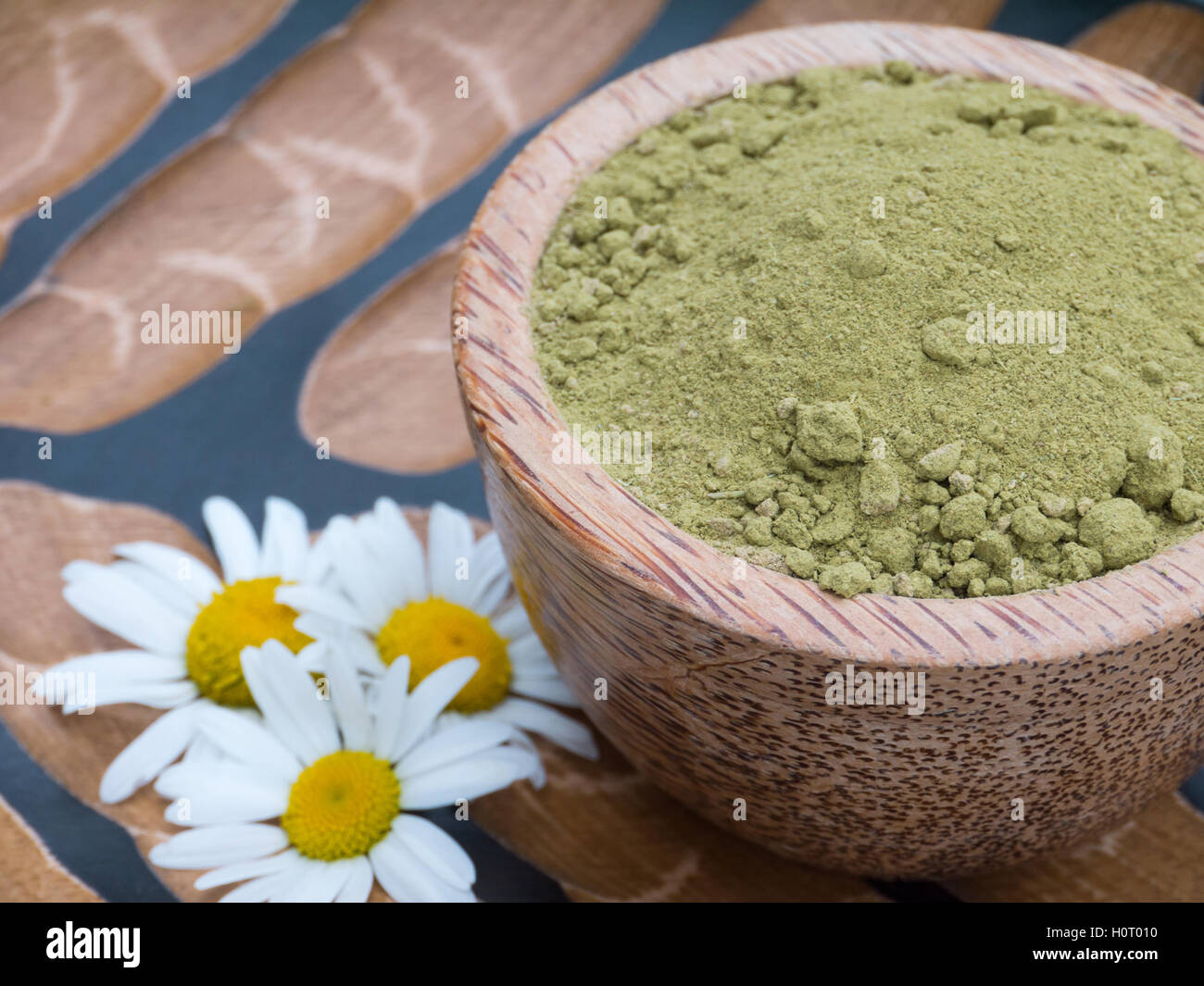 La henna en polvo en el tazón de coco y flores de manzanilla, sobre fondo de textura Foto de stock