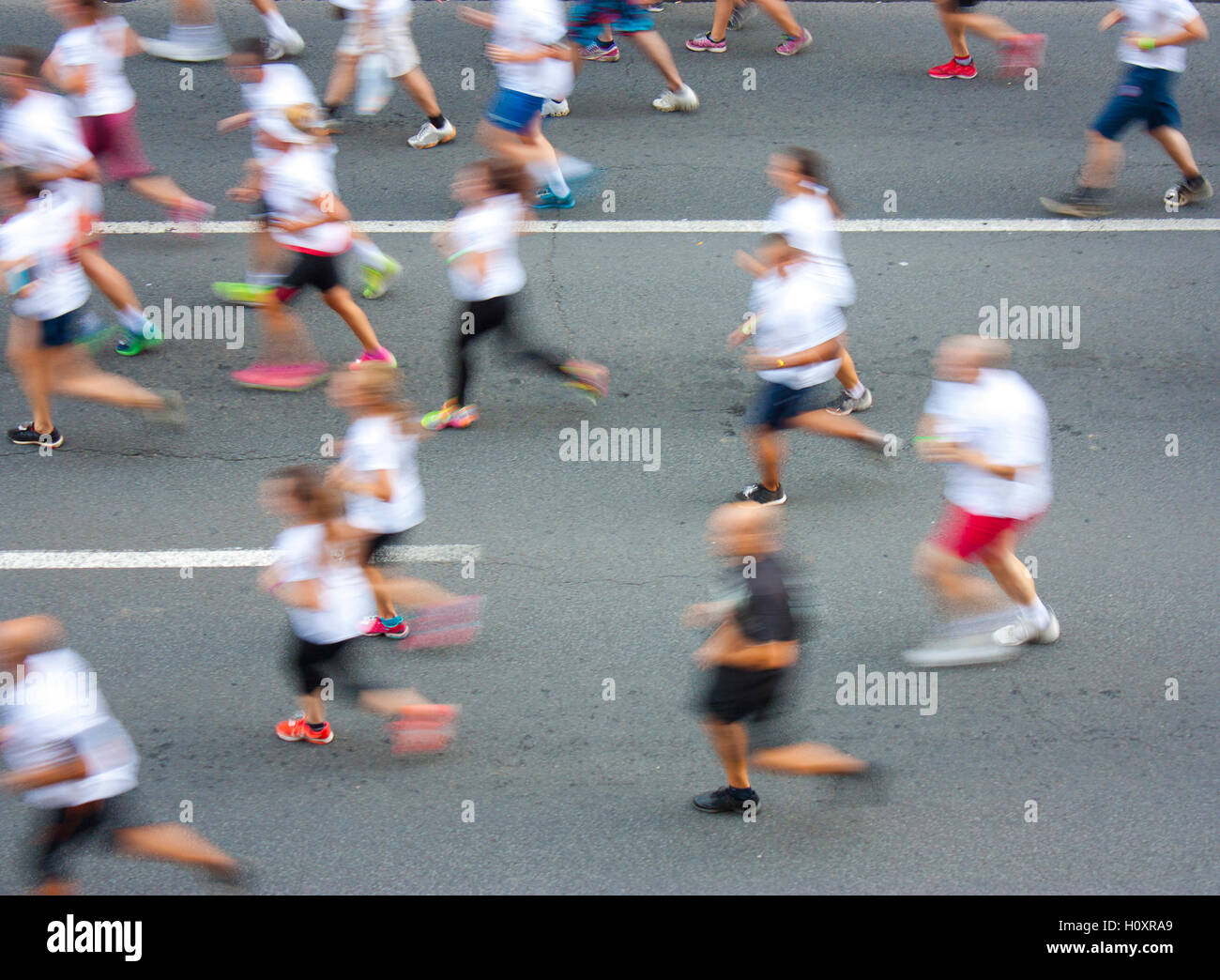 Personas en T-Shirts blancos corriendo media maratón en las calles de la ciudad en el desenfoque de movimiento atencionales Foto de stock
