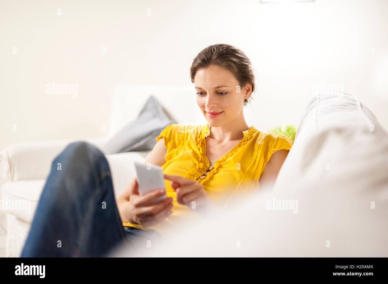 Mujer sentada en un sofá, leer mensajes de texto en el teléfono inteligente. Foto de stock