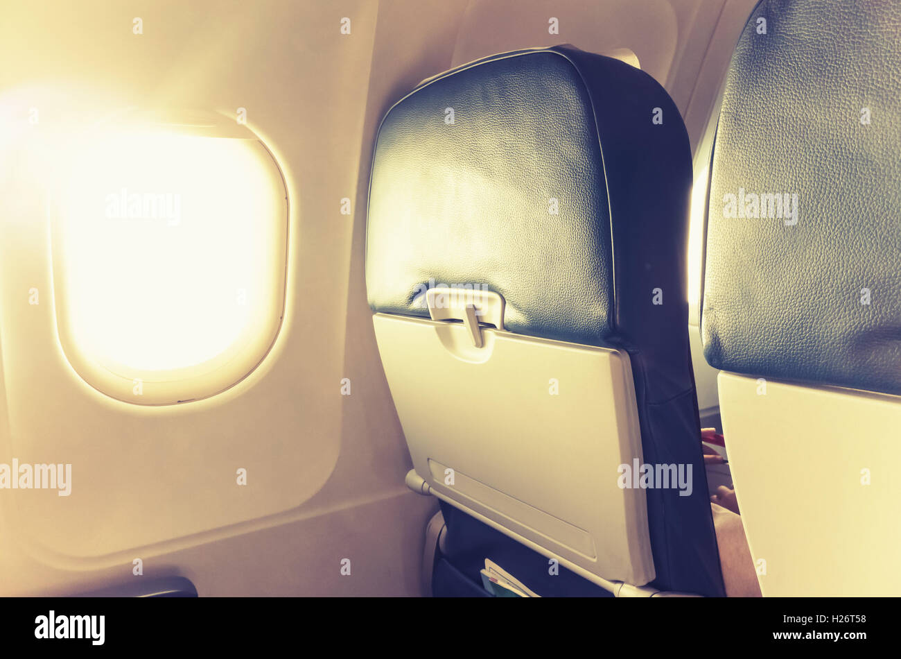 Avión de pasajeros fragmento interior. Cabina principal sillas con mesas plegables y resplandeciente de ojo de buey con luz natural los brillos de la lente. Foto de stock