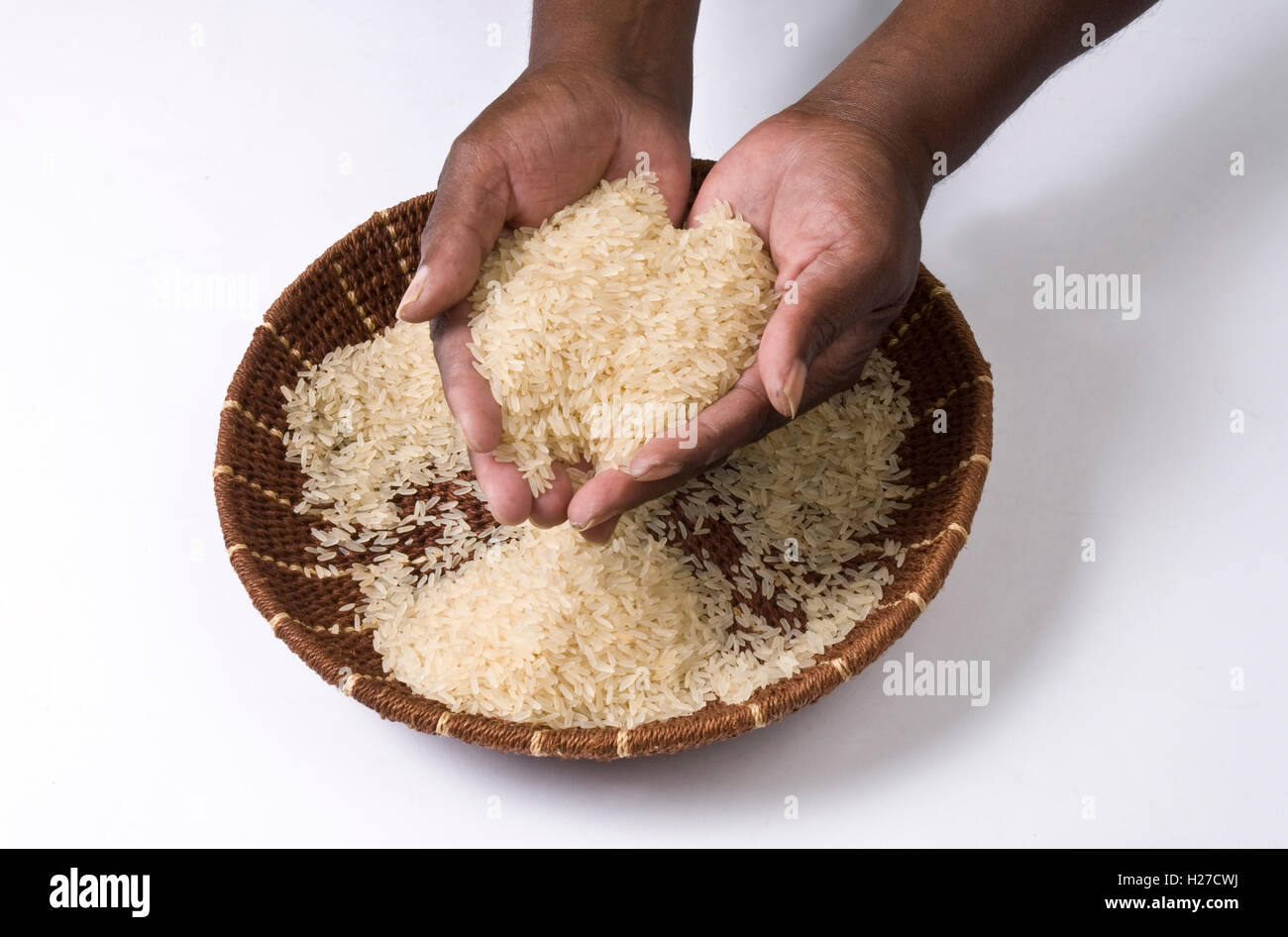 Los africanos manos sosteniendo el arroz en un plato de pasto tejidas a mano. Foto de stock