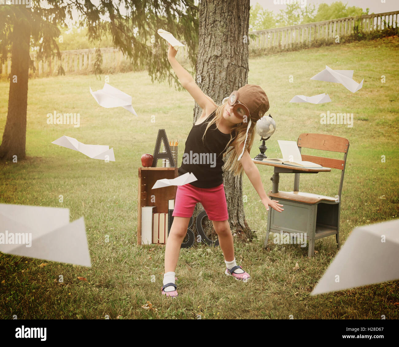 Un niño pequeño está fingiendo ser un piloto de aviones de papel en un aula fuera para una educación o concepto creativo. Foto de stock