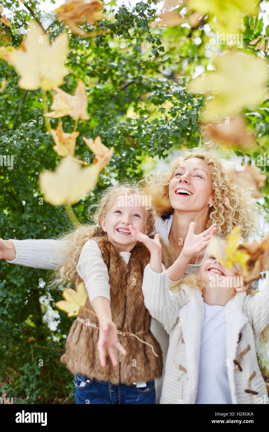 Niños jugando con las hojas de los árboles en el parque con su madre con entusiasmo Foto de stock