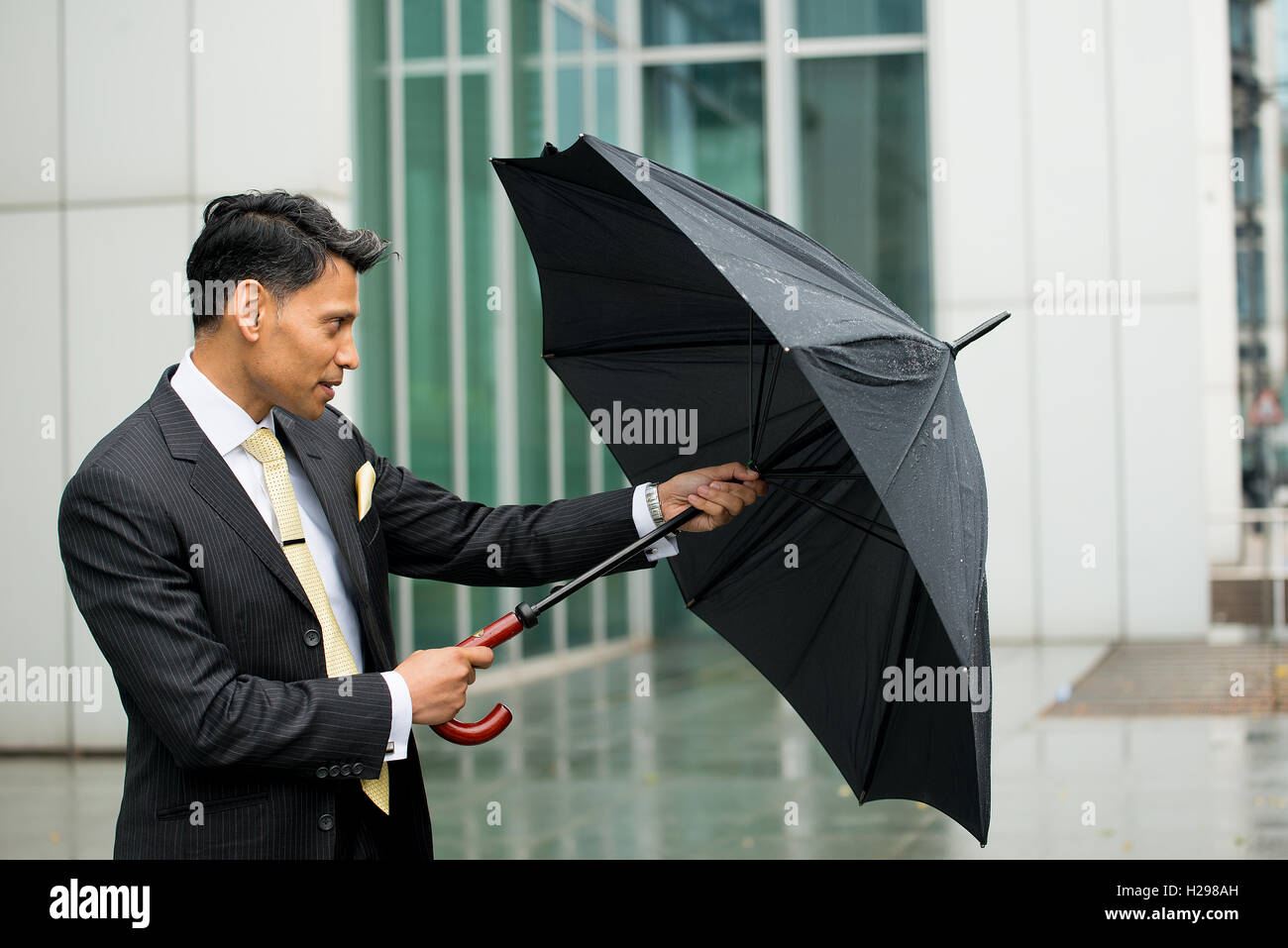 Hombre de negocios luchando para abrir su paraguas antes de que se moje de  la lluvia Fotografía de stock - Alamy