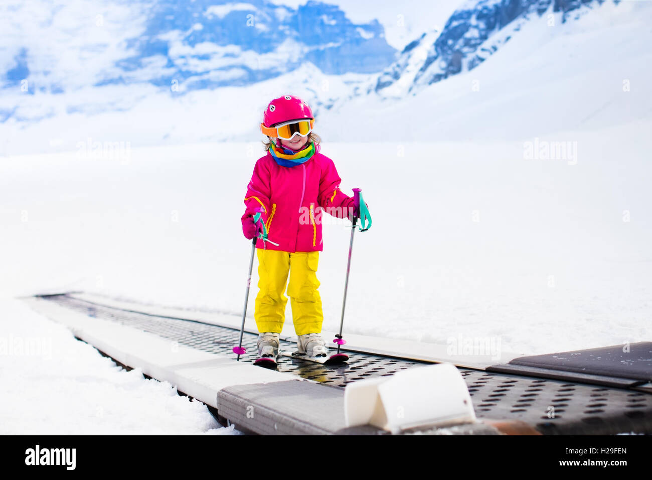 Niño en Magic Carpet ski lift va cuesta arriba en las montañas en invierno  con nieve el día. Los niños en la escuela de deportes de invierno en la  estación alpina Fotografía