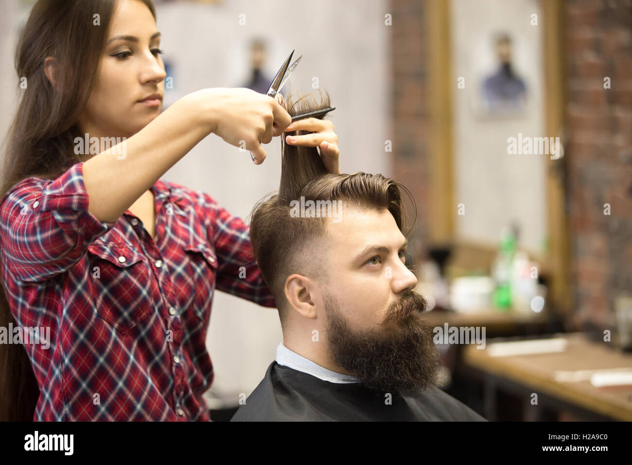 Retrato de apuesto joven barbudo hombre corte de pelo caucásico obteniendo moda moderna en una barbería. Atractiva chica barber trabajando, s Foto de stock