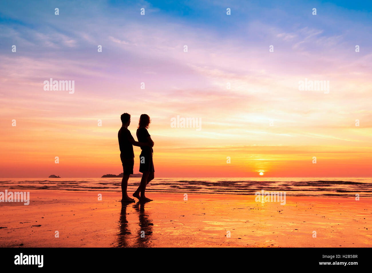 Pareja compartiendo un momento romántico junto a la playa en el atardecer. Foto de stock