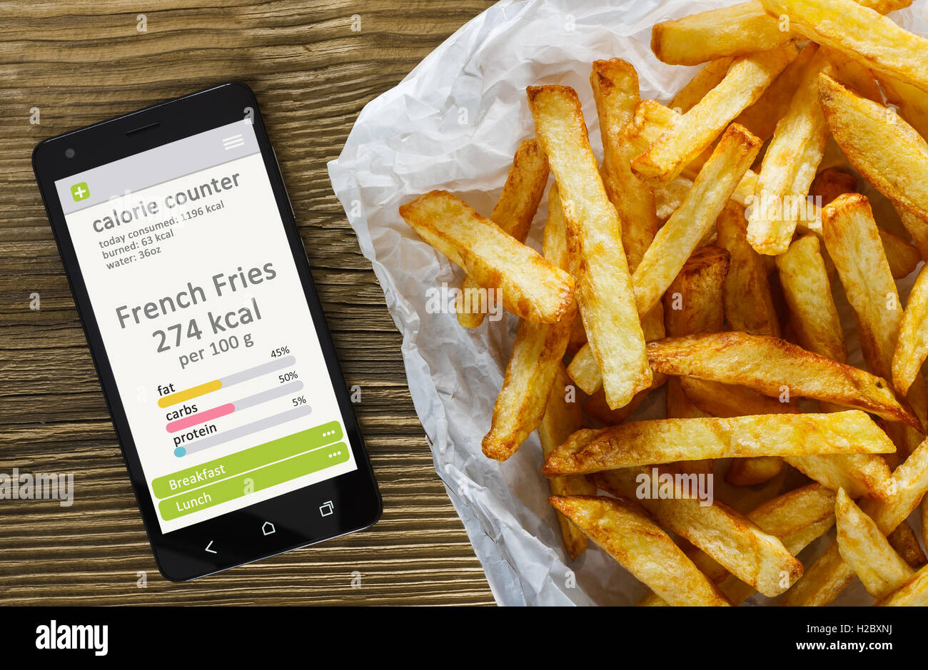 Contador de calorías concepto - teléfono móvil con contador de calorías app en la pantalla y papas fritas. Mesa de madera como fondo Foto de stock