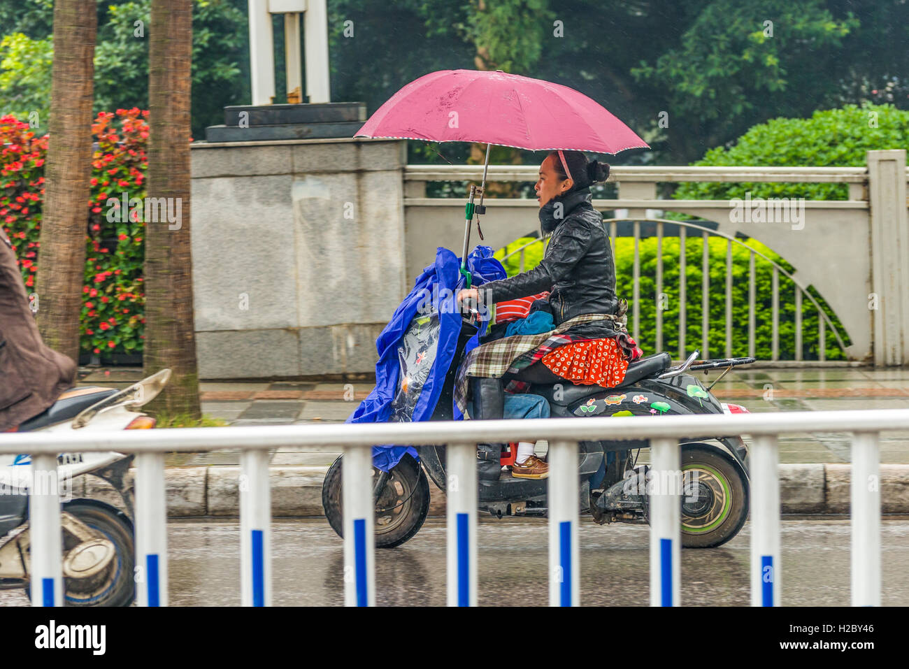 Mujer China con un niño en una moto bajo un paraguas bajo la lluvia en Guilin, China. Foto de stock