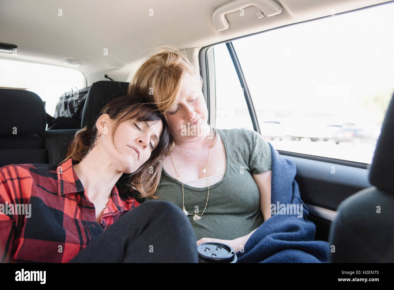 Dos mujeres en un coche en un viaje por carretera, durmiendo en el asiento de atrás, jefes juntos. Foto de stock