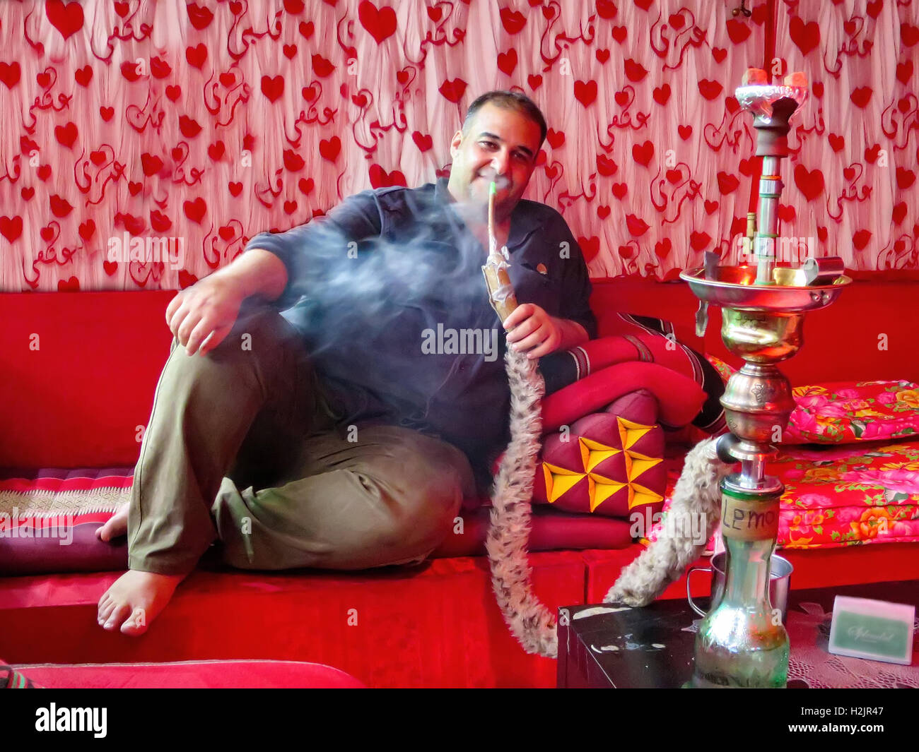 Un hombre iraquí se sienta en un sofá rojo fumar shisha, pipa de agua, en un café de Kuala Lumpur, Malasia. Foto de stock