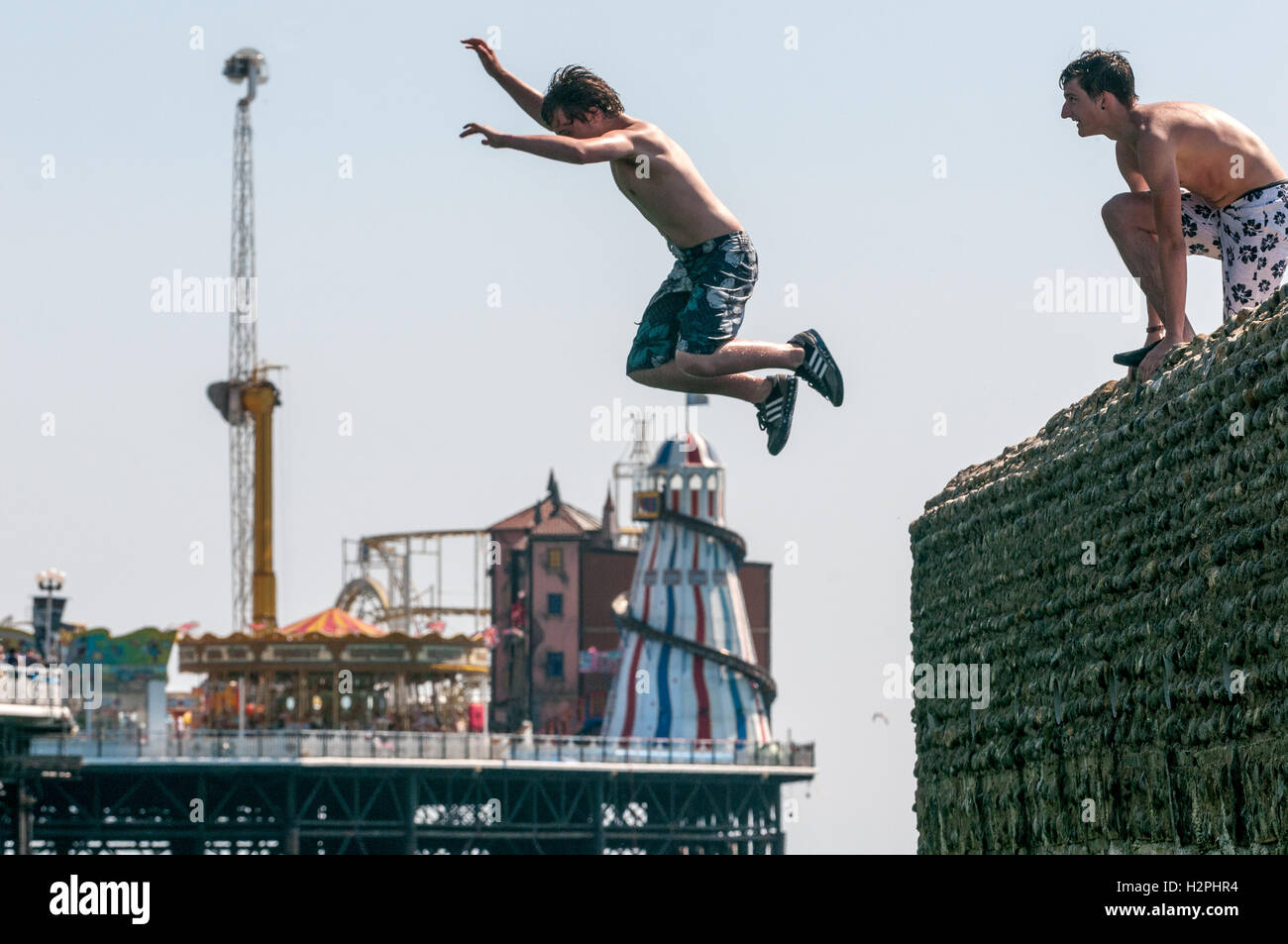 Los adolescentes saltando desde groynes en Brighton Beach en el mar en una tarde caliente. Foto de stock