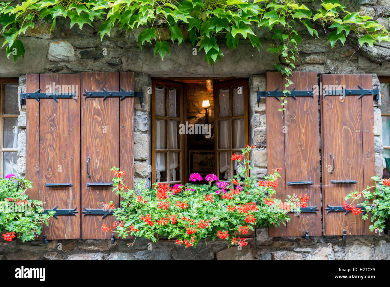 Ivy rodeando una ventana con persianas de flores, cuadro histórico del pueblo medieval de punta de Yvoire, Haute-Savoie, Francia Foto de stock