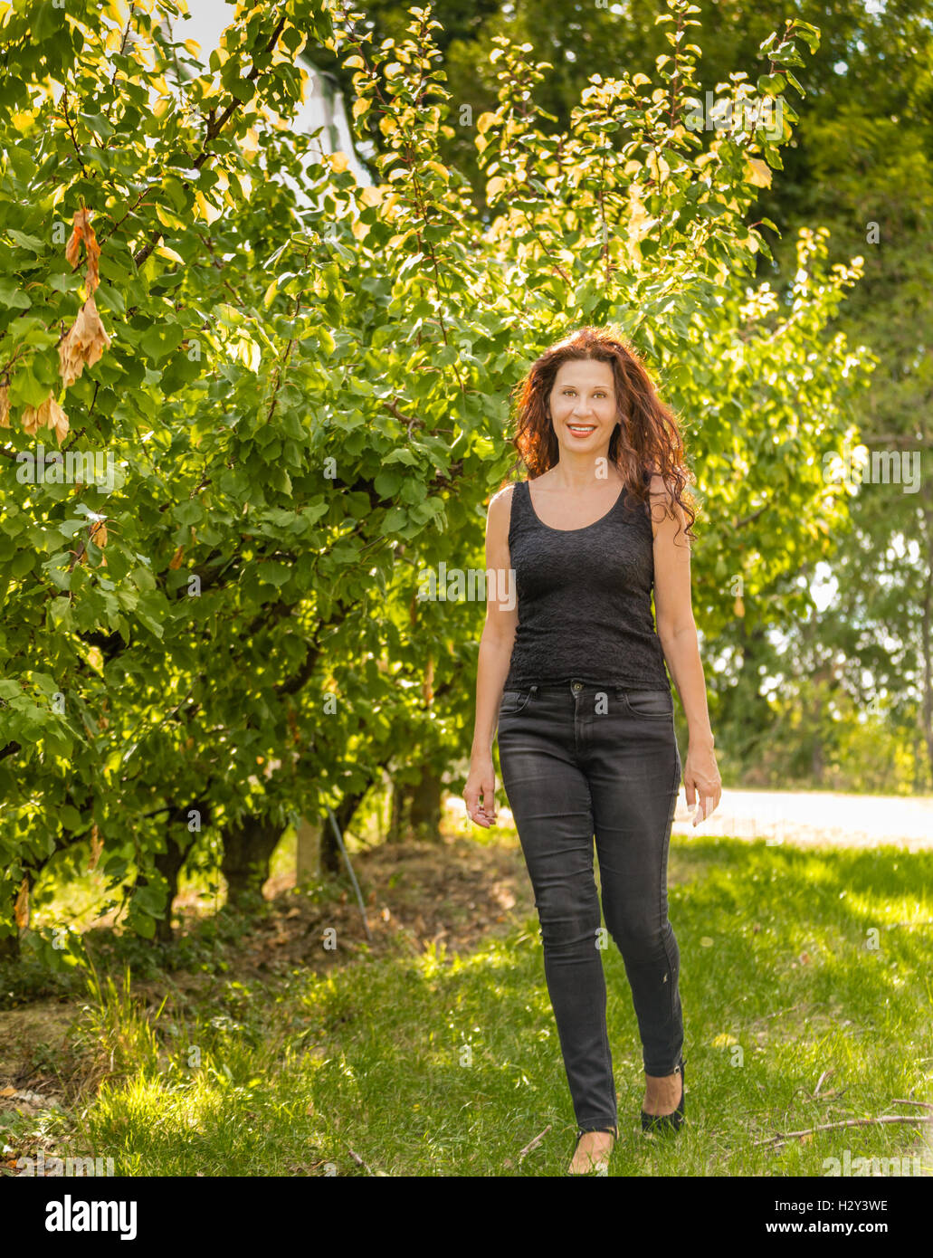 Bonito color rojo mujer disfrutando de la naturaleza de un paisaje mientras camina en el huerto de manzanos en temporada de otoño Foto de stock