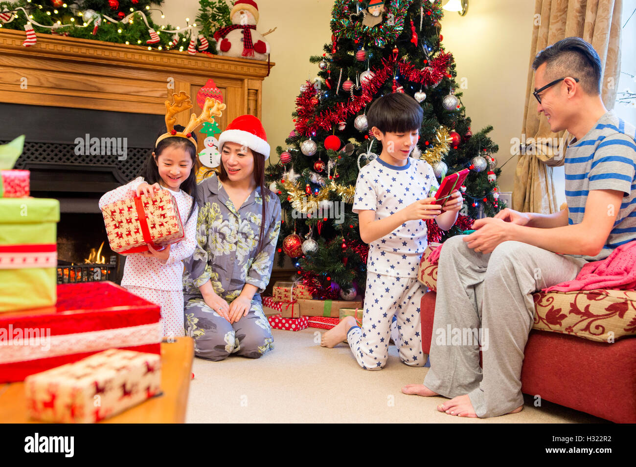 Familia china abriendo regalos juntos en la mañana de Navidad. Están todos sentados en la sala delantera en su pijama Foto de stock