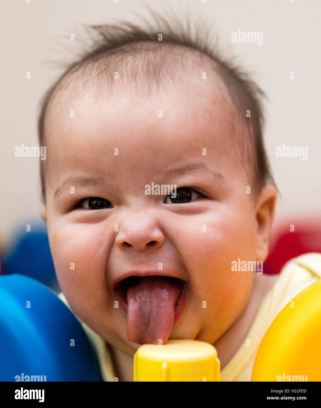 Bebé con divertida sonrisa lamiendo postes de plástico en el corralito Foto de stock
