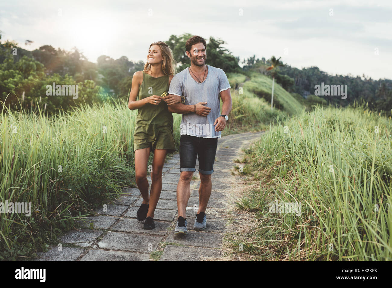 Disparó al aire libre de pareja joven en amor caminando en el camino a través del campo de hierba. Un hombre y una mujer caminando por el pasto alto campo. Foto de stock