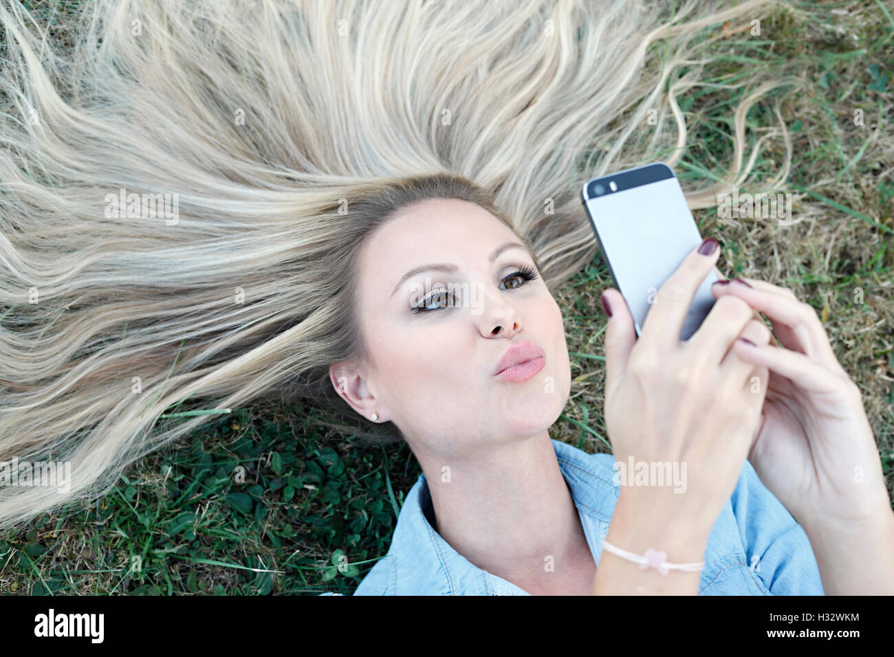 Hermosa joven rubia acostada en la hierba y tomando selfie Foto de stock