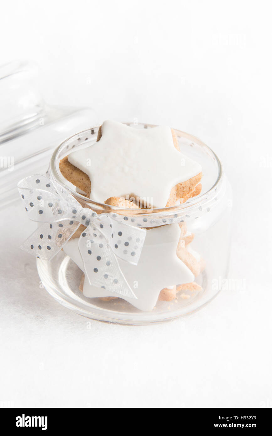 Cerca de un tarro de vidrio lleno con galletas caseras de navidad estrella blanca sobre fondo esponjosas. Foto de stock