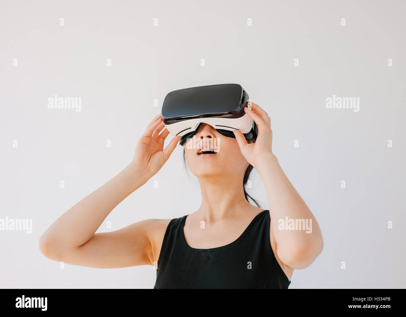 Mujer asiática con el casco de realidad virtual y apartar la mirada. Hembra que lleva puestas las gafas de RV contra un fondo gris. Foto de stock