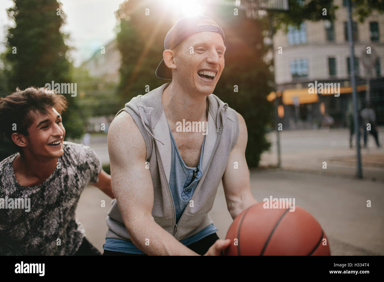Dos jóvenes amigos jugando y divirtiéndose. Streetball jugadores tienen un juego de básquetbol en la cancha al aire libre. Foto de stock