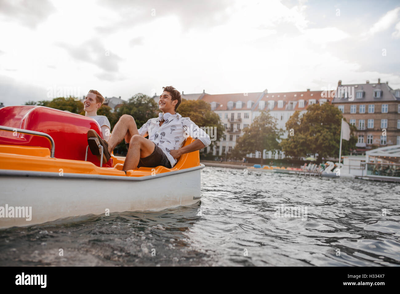 Afuera, tiro de dos jóvenes amigos sentado en bote a pedal. Los chicos adolescentes disfrutar de paseos en bote en el lago. Foto de stock
