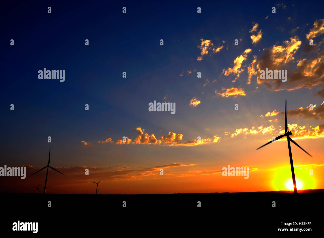 El molino de viento con la puesta de sol y nubes generando electricidad y energía sostenible Foto de stock