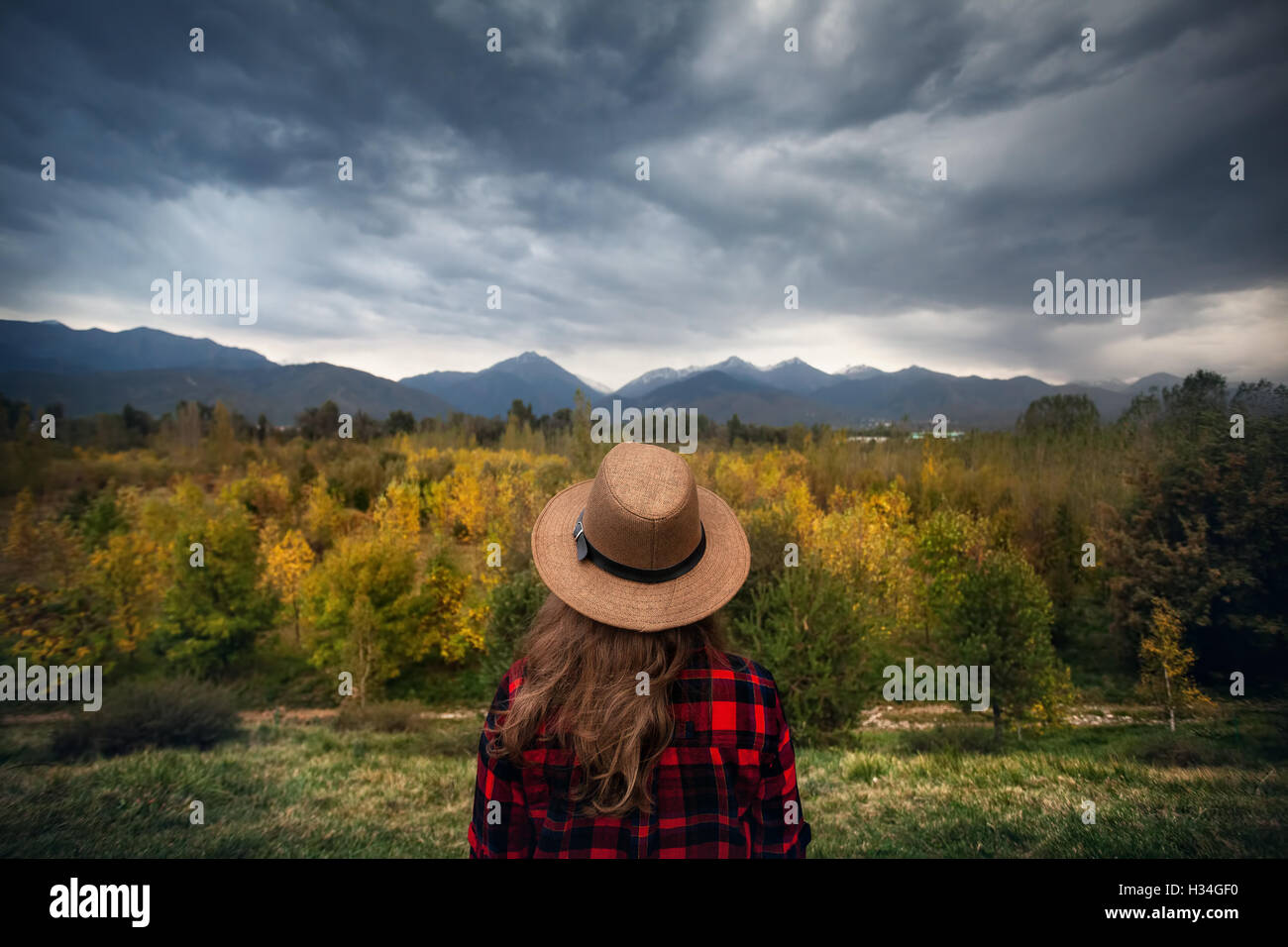 Camisa de cuadros para la mujer en rojo y sombrero mirando el otoño del bosque y las montañas de fondo. Concepto de viaje. Foto de stock