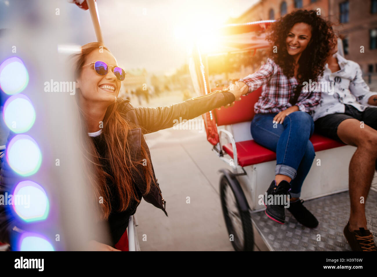Mejores amigos disfrutando de triciclo de paseo en la ciudad. Las adolescentes a caballo en triciclos y tomados de la mano. Foto de stock