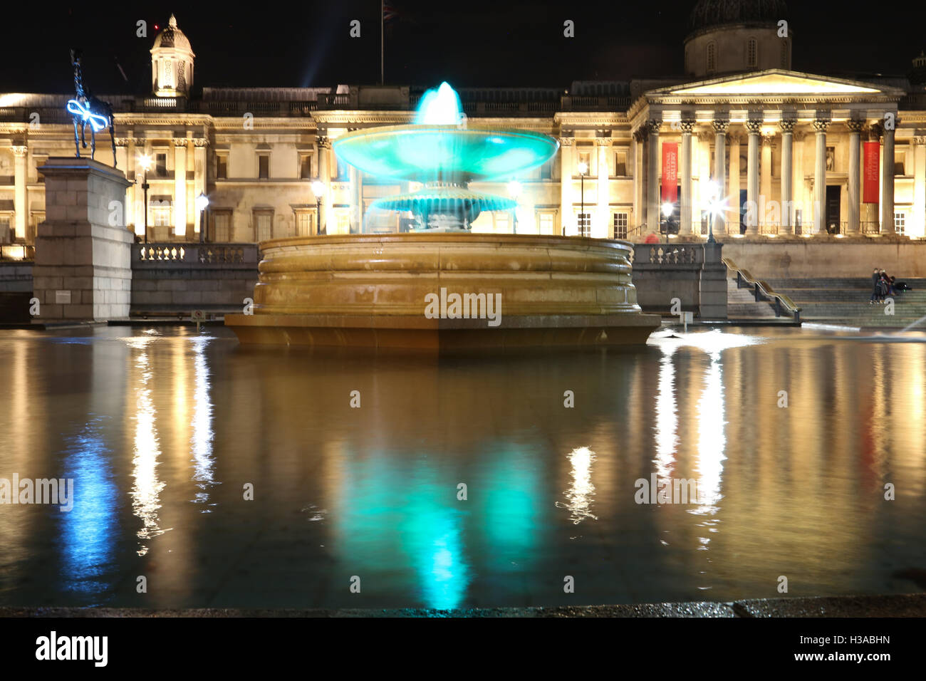 Trafalgar Square y la National Gallery de Londres por la noche, con luces y reflexiones sobre la superficie de la fuente. Foto de stock