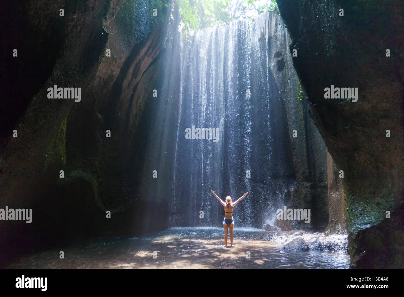 Mujer alegre y viajero con brazos levantados disfrutando de la vida en una hermosa selva cascada en Bali Foto de stock