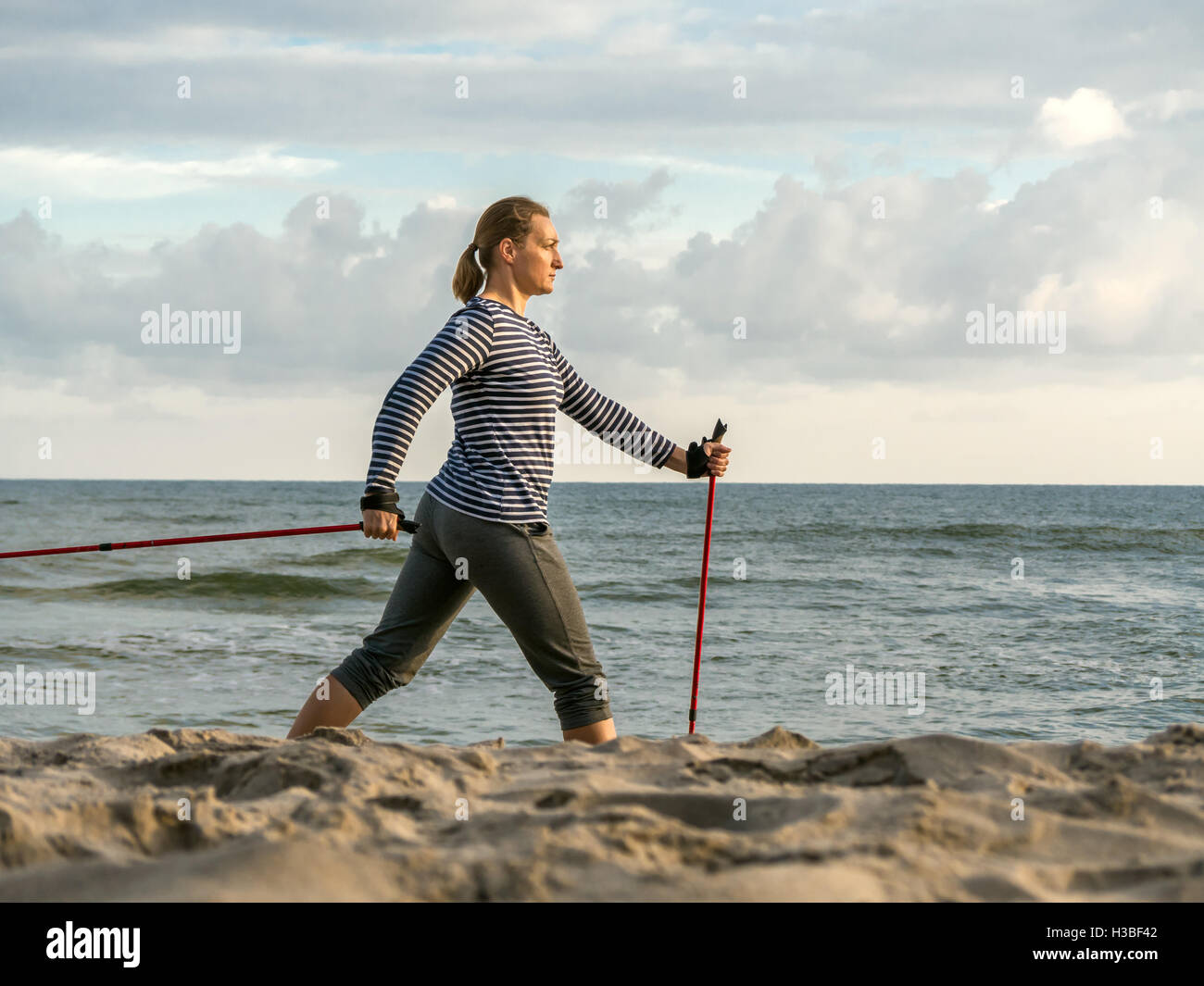 Mujer joven practicando nordic walking a lo largo de la playa Foto de stock