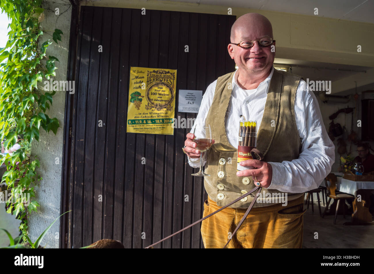 Un hombre en lederhosen llevaba una caja de cigarros y un vaso de vino blanco, Riesling Weingut Erhard Bartz, Enkirch, Mosel, Alemania Foto de stock
